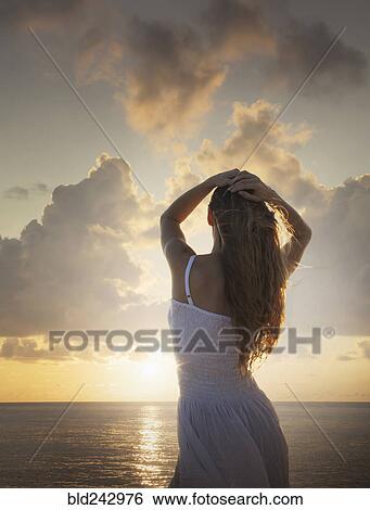 Stock Photograph - Caucasian woman admiring sunset at ocean. Fotosearch