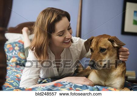 Stock Photo - Caucasian woman and dog laying on bed. Fotosearch