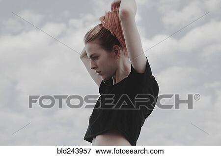 Stock Photo - Caucasian woman arranging hair against clouds. Fotosearch