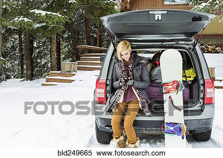 Stock Photography - Caucasian woman at car texting on cell phone in winter. Fotosearch