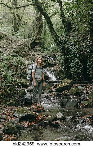 Stock Photo - Caucasian woman backpacking across forest stream. Fotosearch