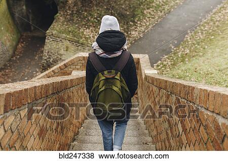Stock Photo - Caucasian woman carrying backpack descending staircase outdoors. Fotosearch