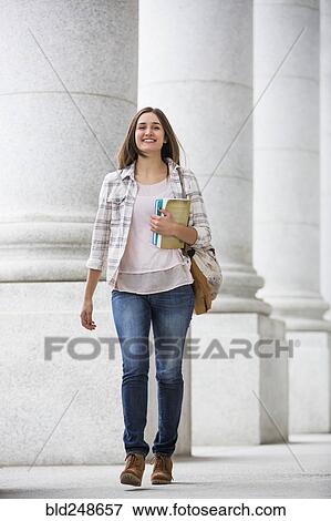 Stock Photo - Caucasian woman carrying books and backpack at school. Fotosearch