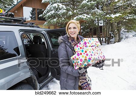 Stock Image - Caucasian woman carrying gifts from car in winter. Fotosearch