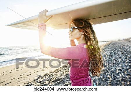Picture - Caucasian woman carrying surfboard on beach. Fotosearch