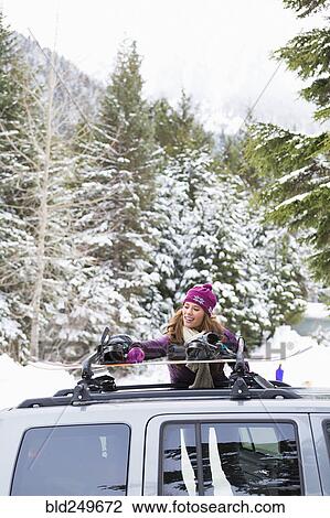 Stock Image - Caucasian woman checking snowboards in car roof rack. Fotosearch