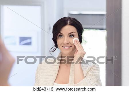 Stock Image - Caucasian woman cleaning face with pad in mirror. Fotosearch