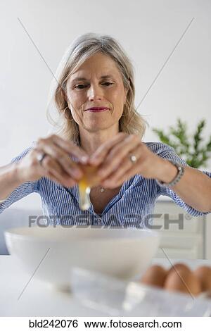 Stock Photograph - Caucasian woman cracking egg into bowl. Fotosearch