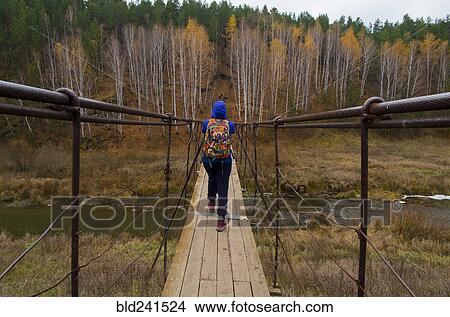 Picture - Caucasian woman crossing river on wooden footbridge. Fotosearch
