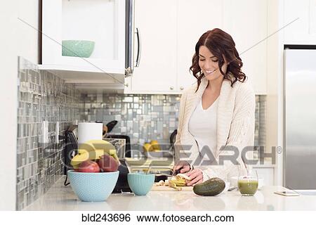Stock Photograph - Caucasian woman cutting fruit in domestic kitchen. Fotosearch