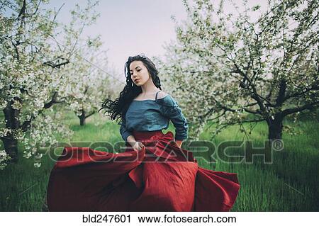 Stock Image - Caucasian woman dancing near flowering trees. Fotosearch