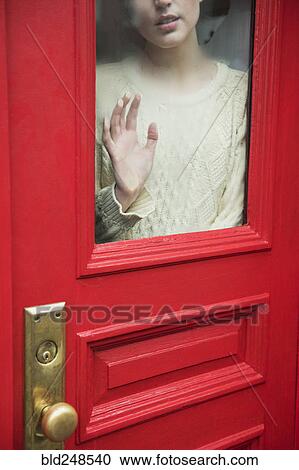 Stock Image - Caucasian woman daydreaming behind red door. Fotosearch