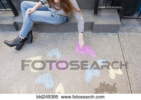 Stock Photography - Caucasian woman drawing hearts with chalk on sidewalk. Fotosearch