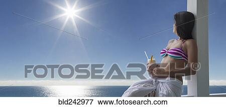 Stock Photo - Caucasian woman drinking cocktail at ocean. Fotosearch