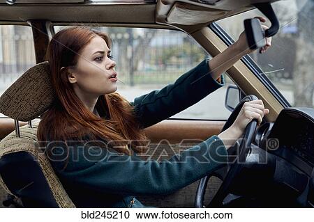 Stock Image - Caucasian woman driving car adjusting mirror. Fotosearch