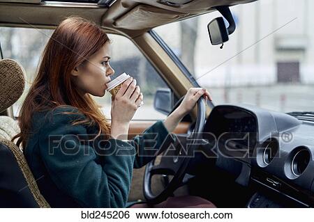 Stock Photograph - Caucasian woman driving car and drinking coffee. Fotosearch