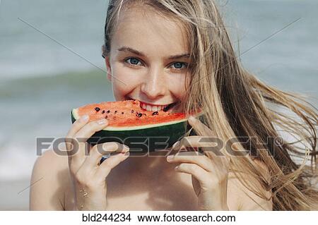 Picture - Caucasian woman eating watermelon on beach. Fotosearch