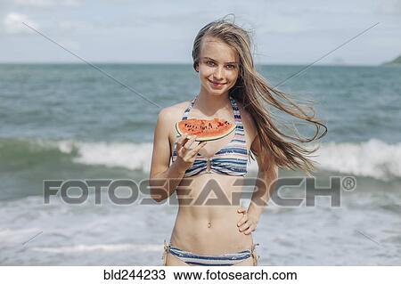 Stock Image - Caucasian woman eating watermelon on beach. Fotosearch