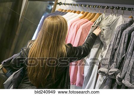 Stock Photo - Caucasian woman examining jeans in clothing store. Fotosearch