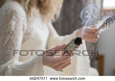 Stock Image - Caucasian woman holding a feather and ritual incense. Fotosearch