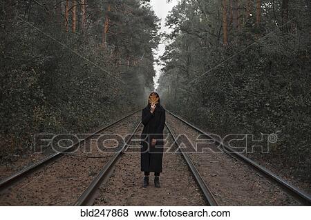 Caucasian woman holding autumn leaf on train tracks in forest View Large Photo Image Stock Photo - Caucasian woman holding autumn leaf on train tracks in forest. Fotosearch