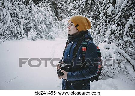 Stock Photography - Caucasian woman holding camera in snowy forest. Fotosearch