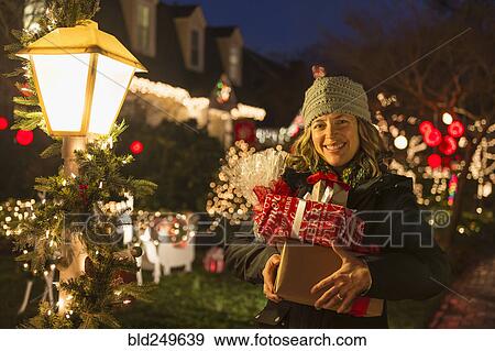 Stock Photo - Caucasian woman holding Christmas gifts on sidewalk. Fotosearch