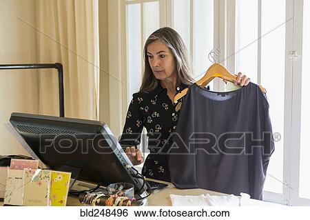 Caucasian woman holding clothing using computer View Large Photo Image Stock Photograph - Caucasian woman holding clothing using computer. Fotosearch