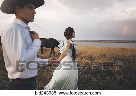 Caucasian woman holding hands with cowboy near river View Large Photo Image Stock Photo - Caucasian woman holding hands with cowboy near river. Fotosearch