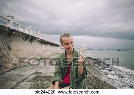 Stock Image - Caucasian woman holding shell at beach. Fotosearch