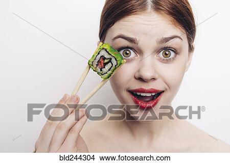 Picture - Caucasian woman holding sushi with chopsticks. Fotosearch