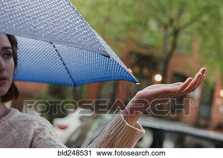 Stock Image - Caucasian woman holding umbrella checking rain. Fotosearch