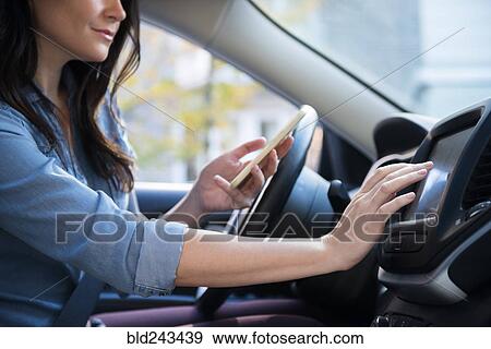 Stock Photo - Caucasian woman in car holding cell phone programming journey. Fotosearch