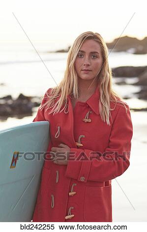 Stock Photography - Caucasian woman in coat carrying surfboard on beach. Fotosearch