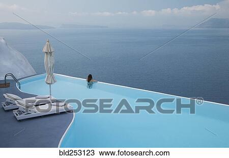 Stock Image - Caucasian woman in infinity pool admiring scenic view of ocean. Fotosearch