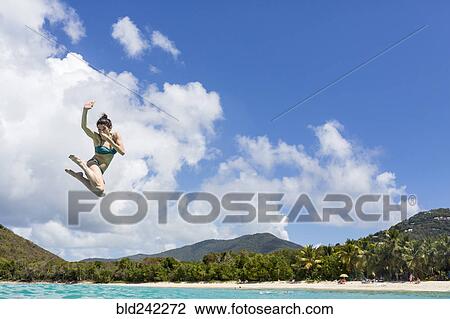 Stock Image - Caucasian woman jumping into tropical ocean. Fotosearch