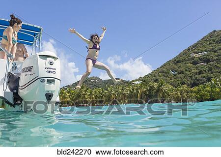 Stock Image - Caucasian woman jumping off boat in tropical ocean. Fotosearch