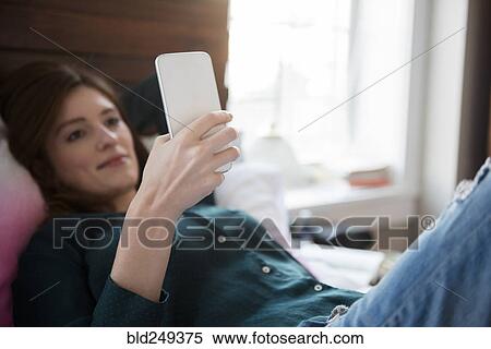 Caucasian woman laying in bed texting on cell phone View Large Photo Image Stock Photography - Caucasian woman laying in bed texting on cell phone. Fotosearch