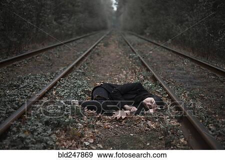 Stock Photo - Caucasian woman laying on autumn leaves near train tracks in forest. Fotosearch