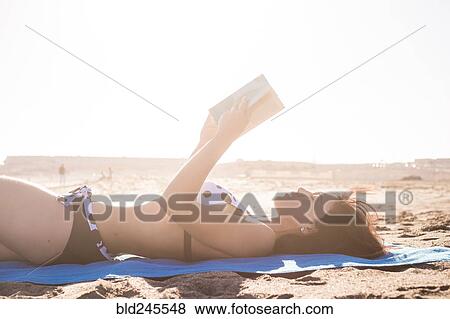 Stock Photo - Caucasian woman laying on beach blanket reading book. Fotosearch