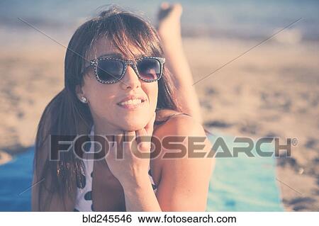 Stock Photograph - Caucasian woman laying on beach blanket. Fotosearch