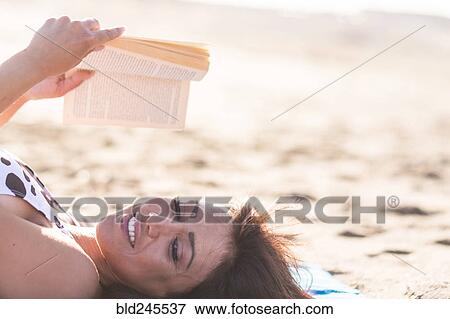 Stock Photo - Caucasian woman laying on beach reading book. Fotosearch