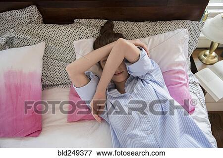 Stock Photo - Caucasian woman laying on bed covering face with arms. Fotosearch