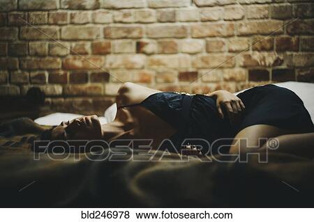 Stock Photo - Caucasian woman laying on bed near brick wall. Fotosearch