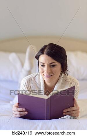 Stock Photo - Caucasian woman laying on bed reading book. Fotosearch