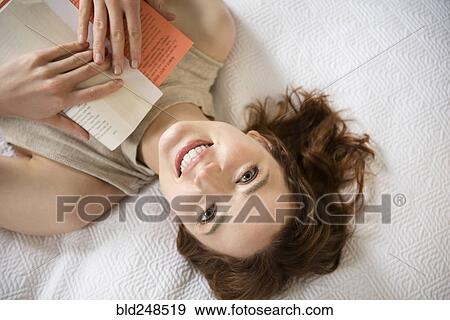 Stock Photo - Caucasian woman laying on bed reading book. Fotosearch