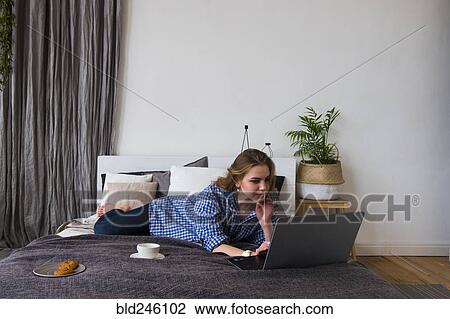 Stock Image - Caucasian woman laying on bed using laptop. Fotosearch