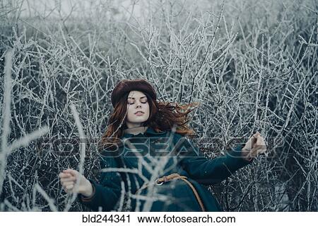 Stock Image - Caucasian woman laying on branches in winter field. Fotosearch