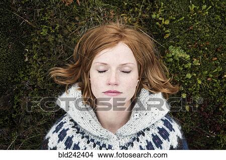 Picture - Caucasian woman laying on moss with eyes closed. Fotosearch