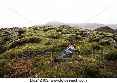 Stock Image - Caucasian woman laying on mossy rocks. Fotosearch